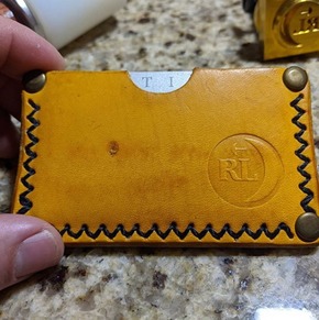 Leather card holder with visible decorative stitching and a logo imprinted using a cold stamp and mallet.
